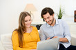 © W PRODUCTION - cheerful young couple on sofa at home websurfing and shopping online with credit card, a laptop computer and internet technology