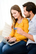 © W PRODUCTION - cheerful young couple on sofa at home websurfing and shopping online with credit card, a laptop computer and internet technology