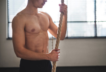 Wall Mural - Fit young man in gym standing topless , holding climbing rope.