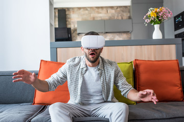 Wall Mural - emotional man wearing virtual reality headset while sitting on sofa at home