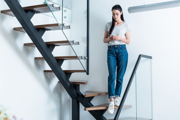 Wall Mural - woman using smartphone while standing on stairs at home