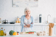 portrait of smiling senior with arms crossed standing at counter with fresh vegetables in kitchen