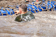 Man swiming in the moat during  a mud race with obstacle course.