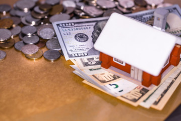 Mortgage house loan, real estate tax, macro financial Concept, Scandinavian house model with pile of banknotes and coins money on brown wooden shiny surface table, with copy space.