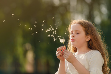 Wall Mural - Cute curly girl blowing dandelion in sunset light.