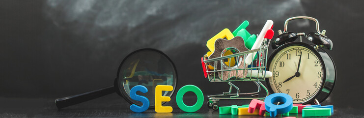 SEO Search engine optimization concept Colored letters of SEO with clock, magnifying , smartphone, gears in a basket on a black background Copy space Banner