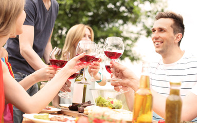 Poster - Young people with glasses of wine at table outdoors. Summer barbecue