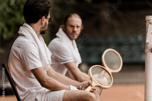 Serious Retro Styled Tennis Players Sitting On Chairs With Towels