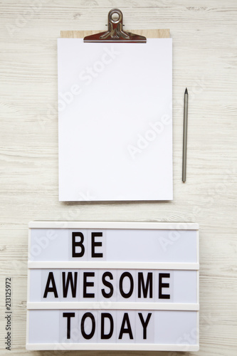 Poster Work space with noticepad, pencil and 'Be awesome today' word on lightbox over white wooden background, top view
