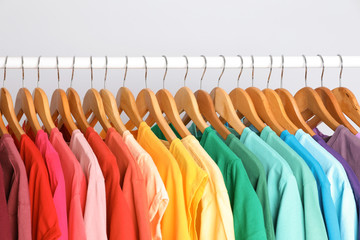 rack with rainbow clothes on light background
