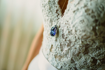 Luxurious blue sapphire jewel dangling from the chest of a bride and her dress.