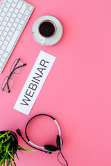 Poster - Business talk, negotiation distantly. Online education. Word webinar on pink office work desk with computer keyboard, headphones, plant, glasses and coffee top view space for text