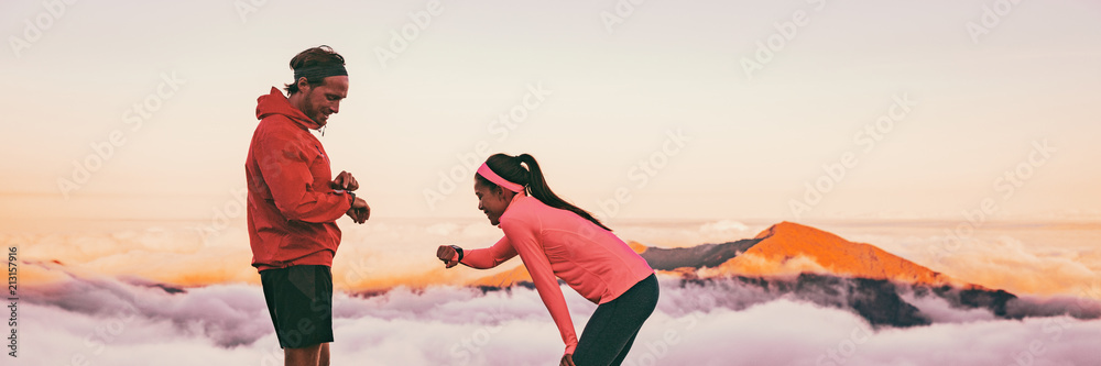 Runners tired breathing after training looking at their wearable tech sports watch checking heart rate health data. Two athletes couple running together in outdoors mountain banner panorama. - obrazy, fototapety, plakaty 