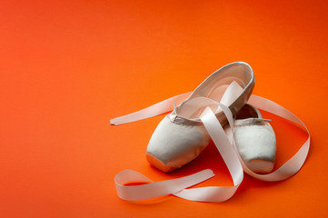 Ballet dancing concept with a pair of silk shoes isolated on minimalist bright orange background