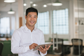 Smiling Asian businessman using a digital tablet in an office