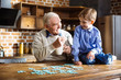 Positive aged man assembling jigsaw puzzle