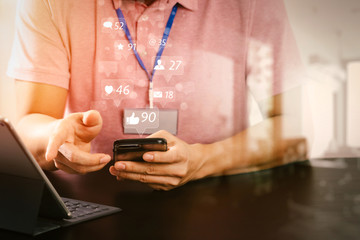 Poster - businessman in pink t-shirt working with smart phone and digitl tablet computer on wooden desk in modern office with glass reflected view