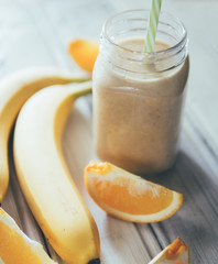 Wall Mural - Fresh banana and orange smoothie on wooden white table