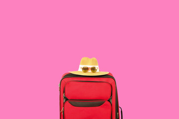 Wall Mural - Single red durable textile luggage with women's straw hat, sunglasses. One suitcase prepared for business trip. Traveling alone concept. bright pink isolated background, copy space for text, close up.