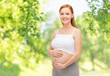 pregnancy, motherhood, people and expectation concept - happy pregnant woman touching her bare belly over green natural background