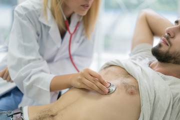 Beautiful woman doctor in white medical coat examines a patient with a stethoscope in hospital. Medical and healthcare concept.