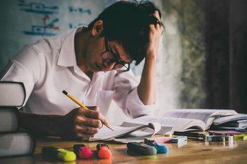 Wall Mural - young asian student man sitting at desk in home studying and reading, doing homework and lesson prac