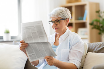 Wall Mural - age and people concept - happy senior woman reading newspaper at home