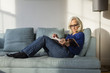 © Cavan Images - Full length of senior woman reading book while resting on sofa at home