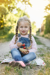 Wall Mural - little girl is sitting on the grass and eating strawberries