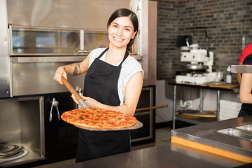 Smiling chef holding big shovel with pizza