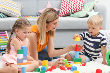 Wall Mural - Young woman and cute children playing with constructor on floor at home