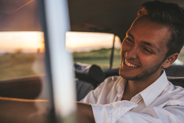 Closeup portrait of handsome happy male driver smiling while sitting in a car with open front window looking to the road during road trip. Caucasian businessman drive a car with toothy healthy smile.