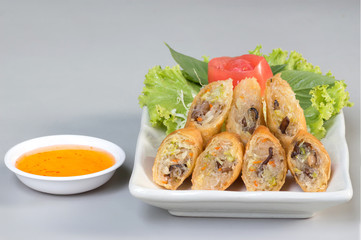 Fried Spring rolls on white dish with sweet sauce on table.