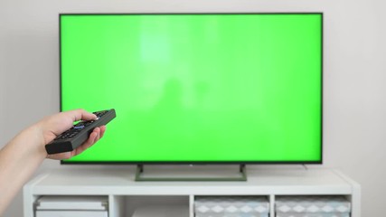 Watching tv with green screen at home interior. Push buttons on remote. Changing channels on television