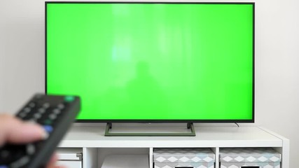 Watching tv with green screen at home interior. Push buttons on remote. Changing channels on television