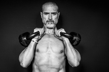 A man 50 Y is holding is raising weights. Black background. Black and white.