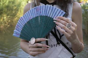 Woman with long fingernails hold fan in the summer park