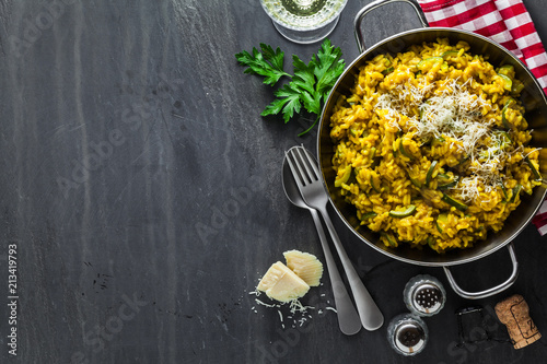 Cuadros en Lienzo Italian dish yellow Risotto milanese with saffron, zucchini and Parmesan cheese on a black slate table with white wine in a glass