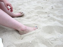 Woman Sitting On The Beach With Her Feet In The Sand 