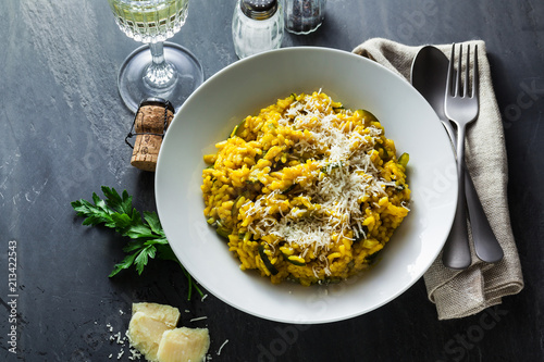 Fotomural Italian dish yellow Risotto milanese with saffron, zucchini and Parmesan cheese on a black slate table with white wine in a glass