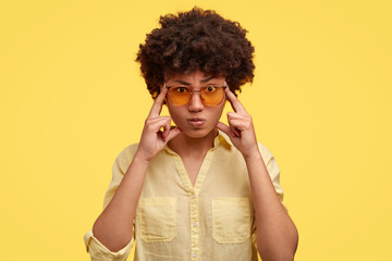 Wall Mural - Serious concentrated African American female student keeps fingers on temples, tries to ease tension, gather with thoughts and remember important information for exam, wears stylish sunglasses