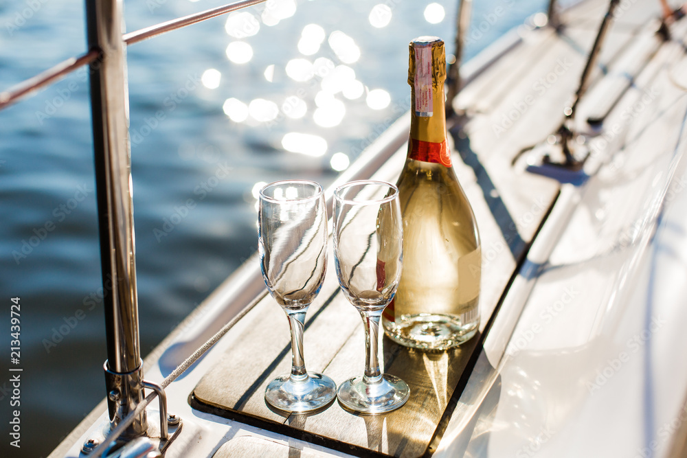 Romantic luxury evening on cruise yacht with champagne setting. Empty glasses and bottle with champagne and tropical sunset with sea background, nobody. - obrazy, fototapety, plakaty 