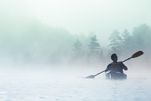 Man Paddling Kayak In Dense Fog In Wilderness Waters