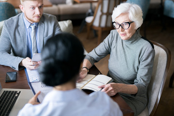 Senior businesswoman writing plans in her notebook and discussing it with her partner at the table