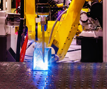Automatic Welding Robot In Modern Factory In Operation Close-up Of Blue And Yellow Flames With Spray.