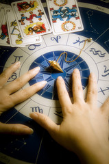 Wall Mural - astrologer, fortune teller with astrology background withd zodiac signs, pendulum and tarot tarots c