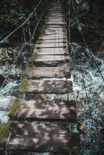 Rickety Rope And Wood Bridge Going Across A Rocky River On A Hiking Trail In The Colcora Valley, Colombia