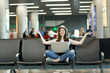 © ViDi Studio - Young relaxed traveler tourist woman with laptop sitting with crossed legs, meditate, spread hands, waiting in lobby hall at airport. Passenger traveling abroad on weekend getaway. Air flight concept.
