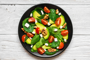 Wall Mural - avocado and spinach salad with tomatoes cherry, feta cheese and walnuts in a plate on rustic wooden table. top view