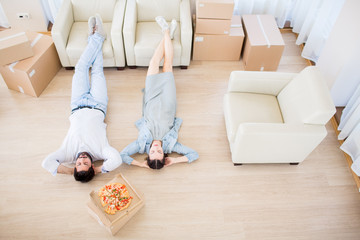 Young relaxed couple lying on the floor with their legs on armchairs after relocation to new house